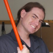 Smiling brown-haired man wearing coveralls and holding a broom